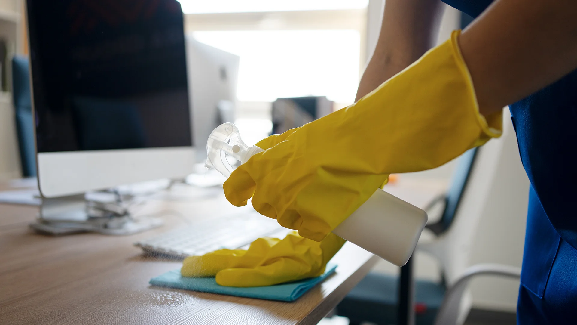 Cleaner sanitising a workplace desk and computer